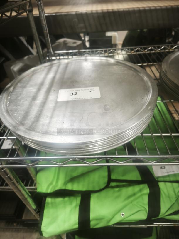 Stack of aluminum pizza pans on a metal shelf, showing slight wear. Label reads "32 QTY, PCIAuctions.com."