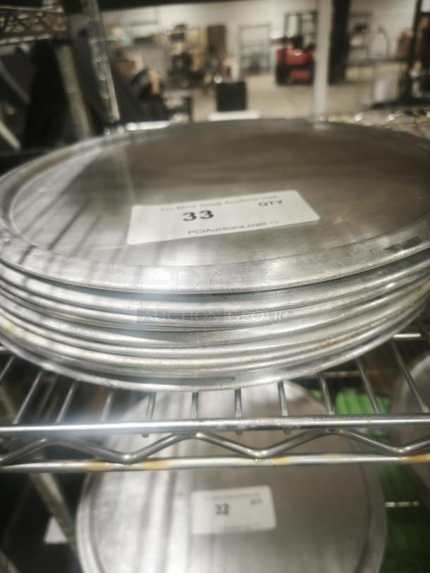 Stack of aluminum pizza pans in good condition on a metal shelf. Label indicates "Quantity: 33," from PGIAuctions.com.