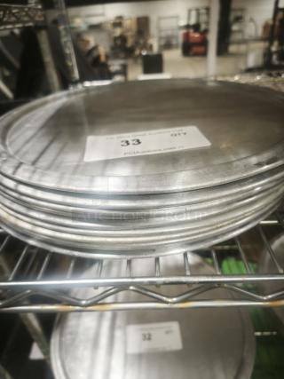 Stack of aluminum pizza pans in good condition on a metal shelf. Label indicates "Quantity: 33," from PGIAuctions.com.