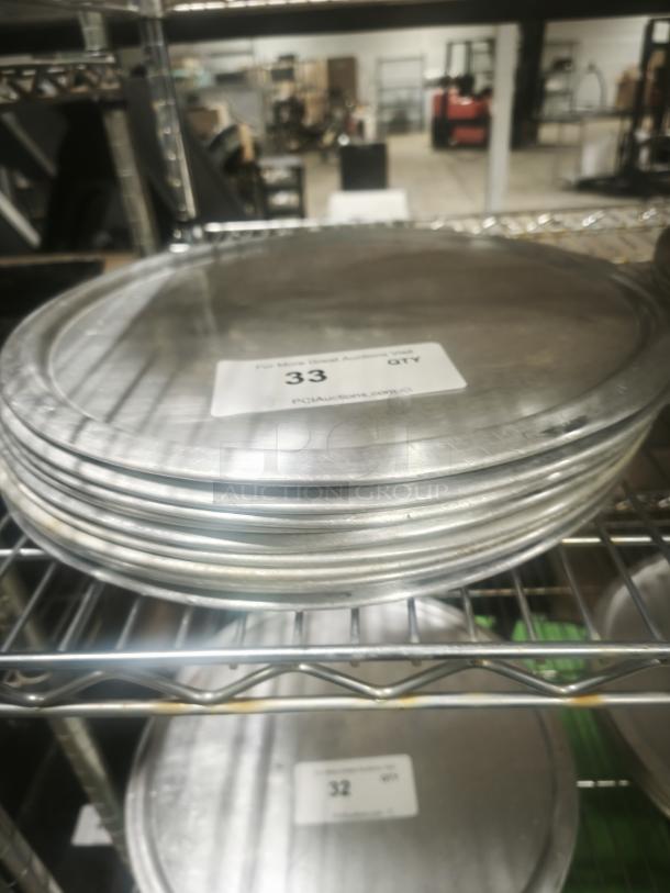 Stack of aluminum pizza pans on a metal rack. Visible label indicates auction lot number 33. Good condition.