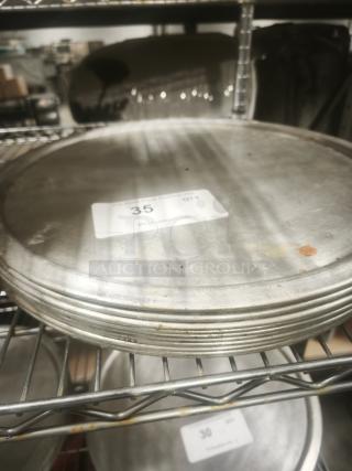 Stack of aluminum pizza pans, good condition, slight wear. Tags show quantity of 35. Stored on metal rack.