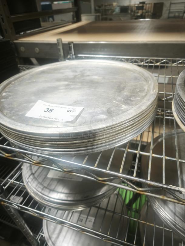 Stack of aluminum pizza pans on a metal rack, showing slight wear. Numbered label "38" visible.