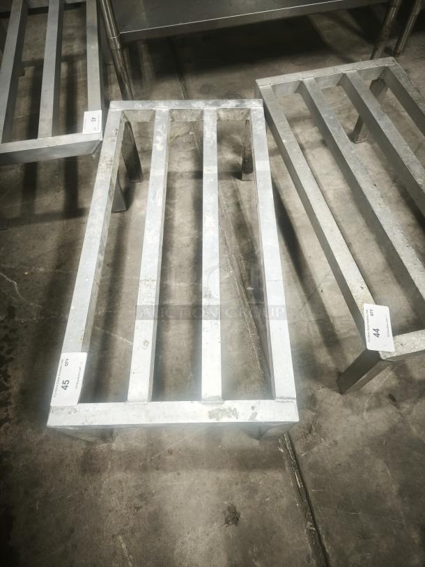 Aluminum dunnage rack for commercial storage, shows used condition with minor wear. Racks are labeled with lot numbers.