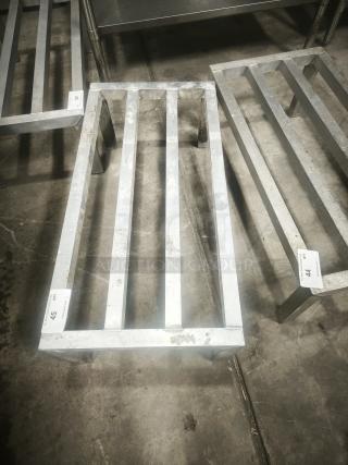 Aluminum dunnage rack for commercial storage, shows used condition with minor wear. Racks are labeled with lot numbers.