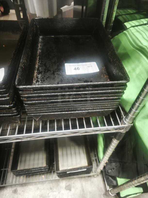 Stack of rectangular enamelware tin plate pans, showing signs of wear, with a visible label marked "46 QTY".