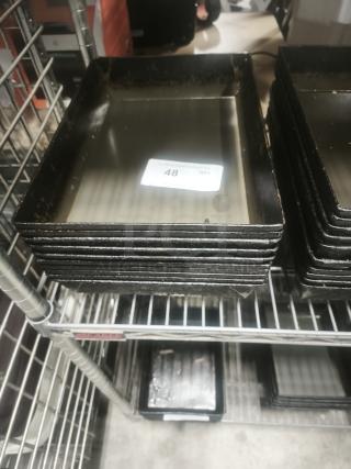 Stack of black enamelware tin plate pans on metal shelving, displaying some wear. Visible tag marked "48 QTY."