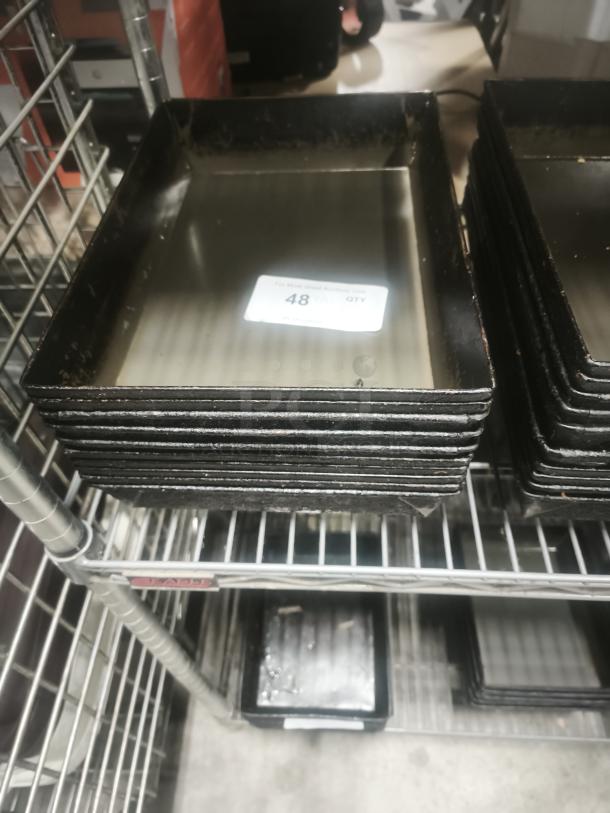 Stack of black enamelware tin plate pans on metal shelf, showing signs of wear. Marked "48" on a sticker.