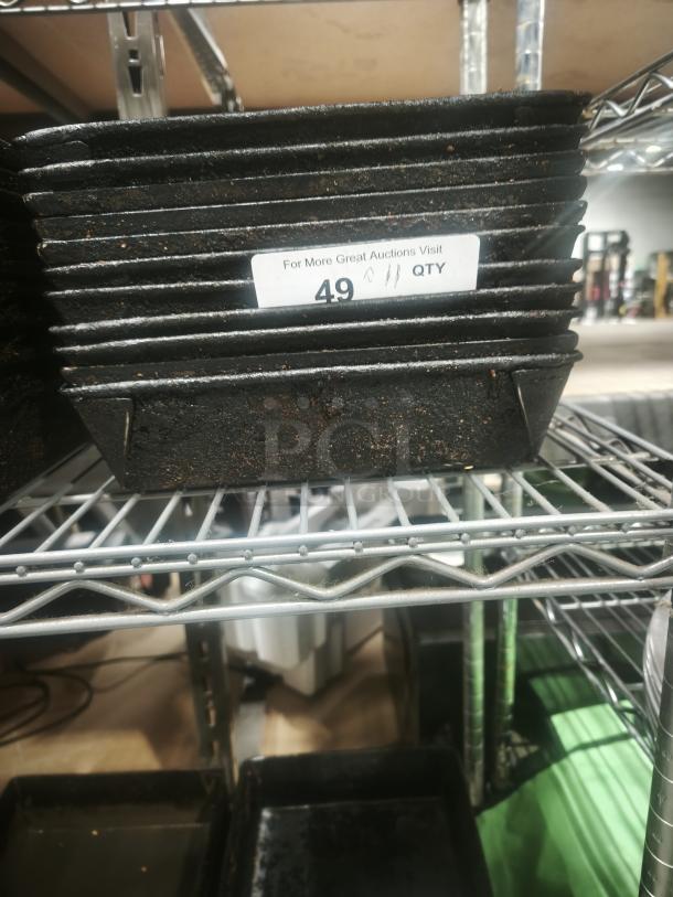 Stacked enamelware tin plate pans with visible surface wear, labeled "49" on a warehouse shelf.