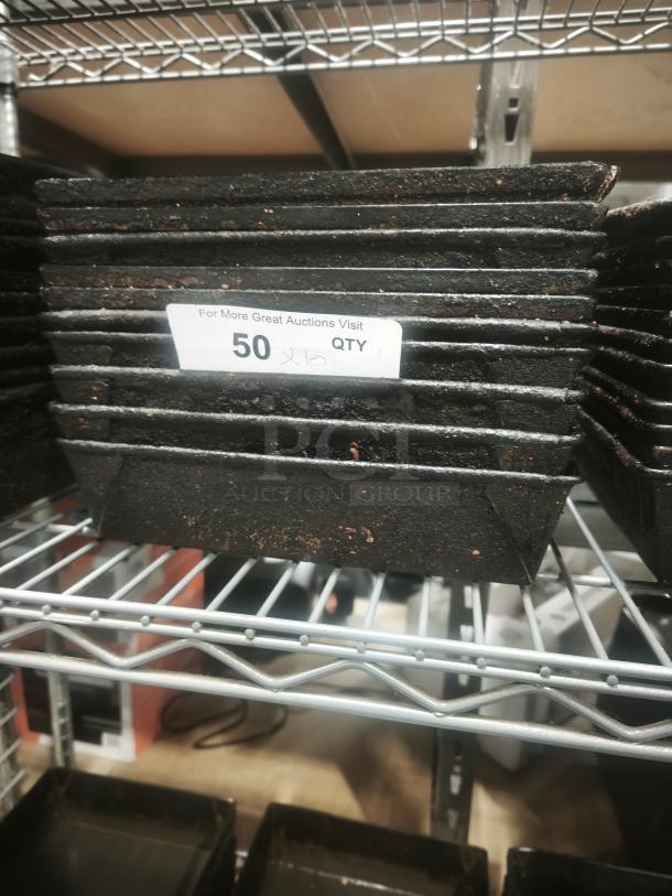 Stack of enamelware tin plate pans with worn surfaces on metal shelves, labeled with "50 QTY."