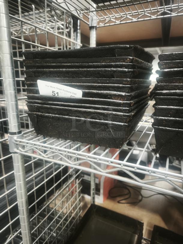 Stack of black enamelware tin plate pans on a metal shelf, showing slight rust. Label reads "For More Great Auctions Visit 51."