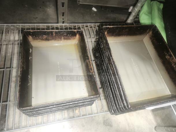 Stack of rectangular enamelware tin plate pans with worn edges, on a metal shelf.