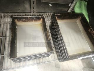 Stack of rectangular enamelware tin plate pans with worn edges, on a metal shelf.