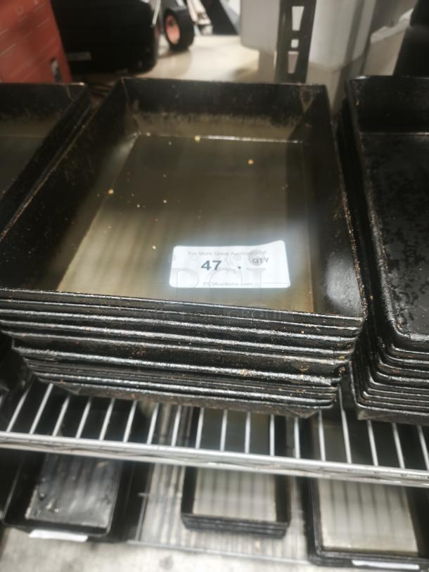 Stack of rectangular enamelware tin plate pans with visible wear, placed on a metal rack. Label indicates quantity as 47.