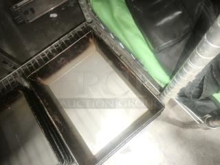 Enamelware tin plate pans with aged patina, rectangular shape, visible wear and rust, stacked on a metal shelf.