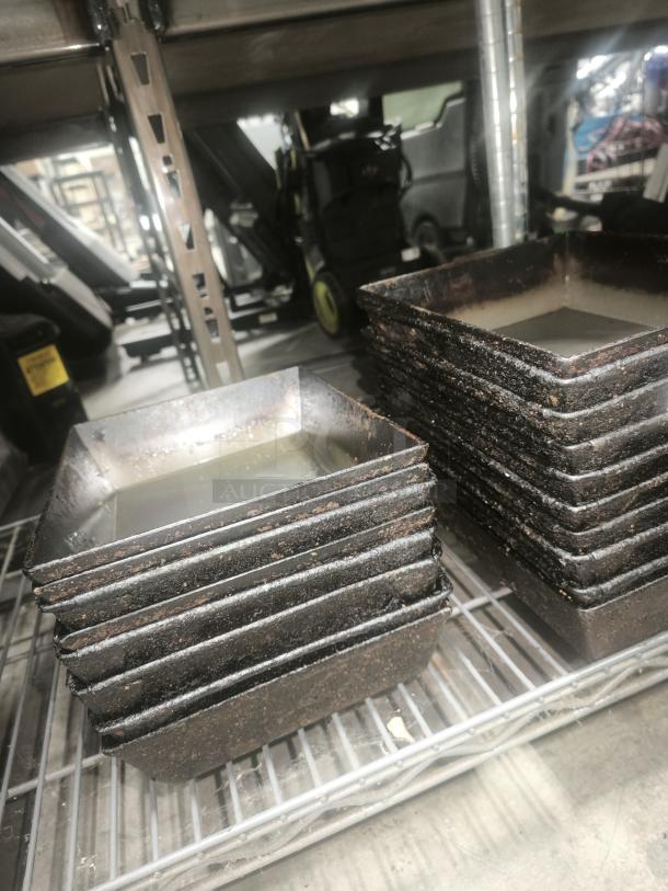 Stacked enamelware tin plate pans on a metal shelf. Rectangular shape with visible wear, used condition.