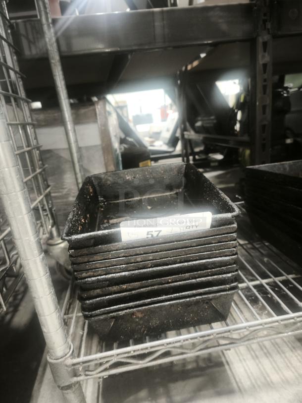 Stack of black enamelware tin plate pans on metal shelf, showing signs of wear, labeled with auction number 57.
