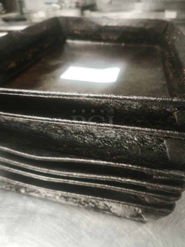 Stack of vintage enamelware tin plate pans with visible wear, showing textured, darkened surfaces, indicating age and use.