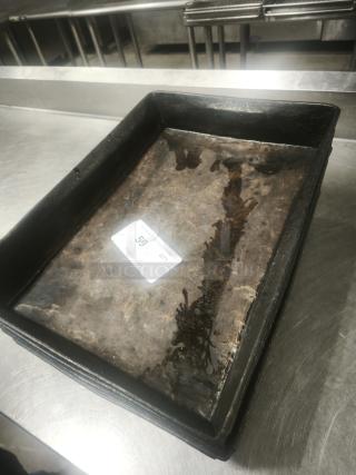 A stack of rectangular enamelware tin plate pans with worn surfaces, showing rust and signs of use. Auction lot tag visible.