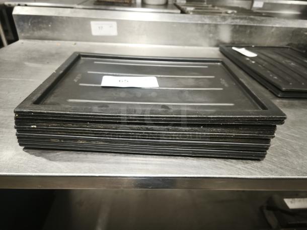 Black plastic tray or lid, stack of eight, rectangular shape, with slight wear. Number tag indicating item 65.
