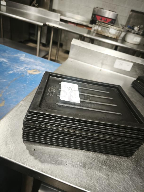 Stack of multi-purpose black plastic trays/lids on a metal surface. Good condition, auction tag visible.