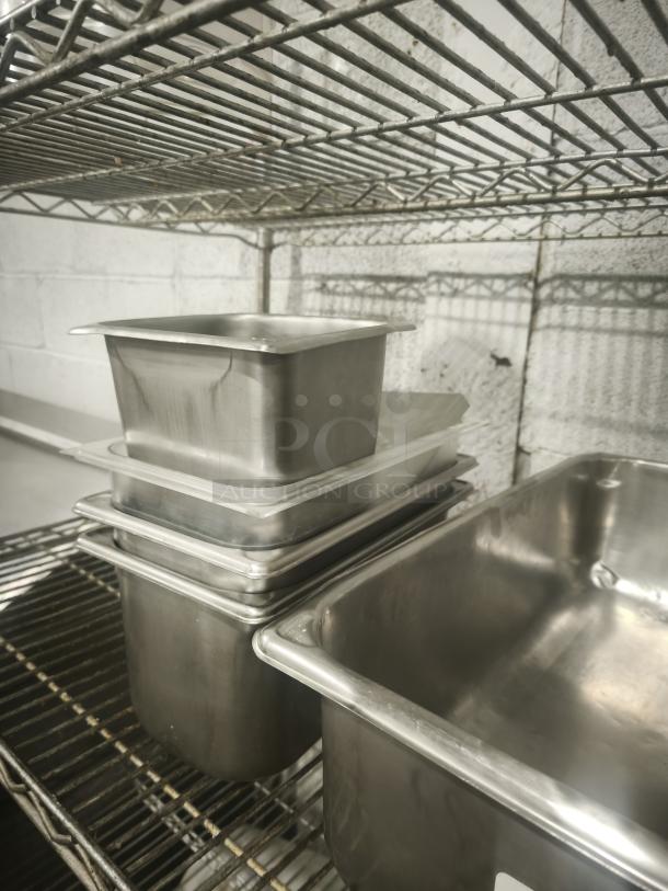 Stainless steel steam pans in mixed sizes, stacked on a wire rack, in good condition.
