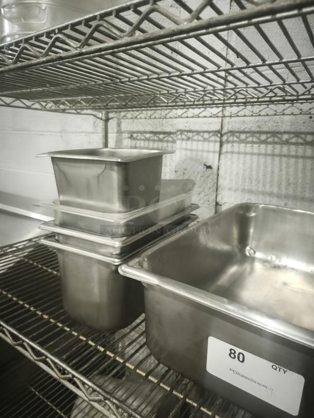 Stainless steel steam pans in mixed sizes, stacked on a metal shelf, showing minor wear. Label reads "80 QTY PCIAuctions.com".