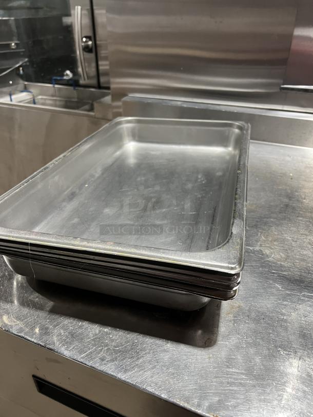 Stack of commercial stainless steel steam table pans, stackable design, in used condition, suitable for professional kitchens.