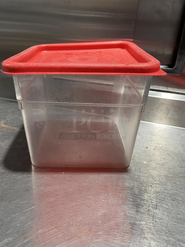 Commercial clear polycarbonate 6 Qt. food storage container with red lid, in good condition, shown on metal surface.
