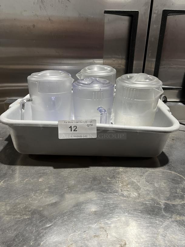 Commercial clear polycarbonate beverage pitchers, set of four, in good condition, shown in a white tray with auction label.
