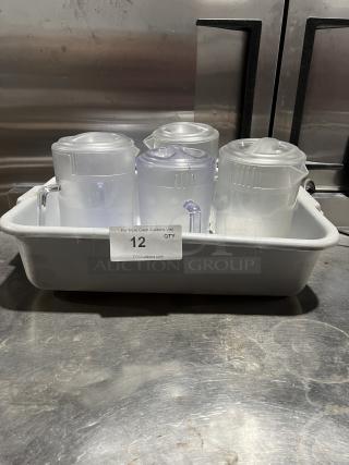 Commercial clear polycarbonate beverage pitchers, set of four, in good condition, shown in a white tray with auction label.