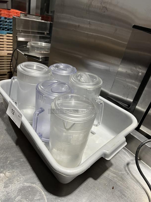 Clear polycarbonate beverage pitchers with lids in a tray. Durable commercial quality. Label shows quantity: 12.