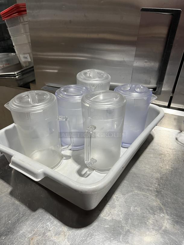 Four clear polycarbonate beverage pitchers with lids, shown in a white tray, suitable for commercial use.