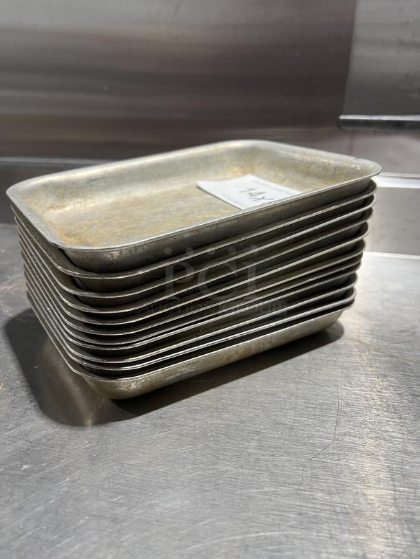 Stack of commercial aluminum baking pans, lightly worn, each labeled "14X" indicating quantity, on metal surface.