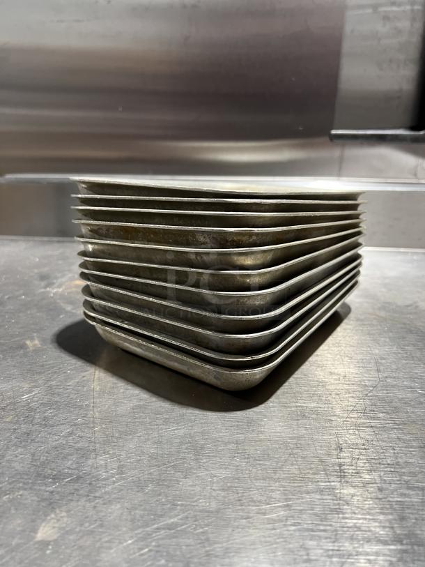 Stack of commercial aluminum baking pans. Used condition, showing mild wear. Auction includes eleven pans.