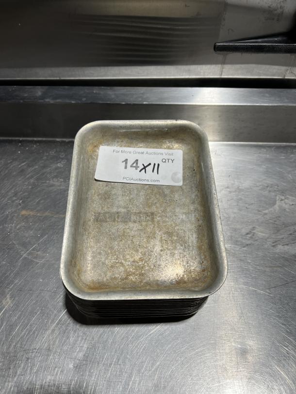 Stack of commercial aluminum baking pans, used, with visible wear. Label reads "14X11 QTY, PCIAuctions.com."