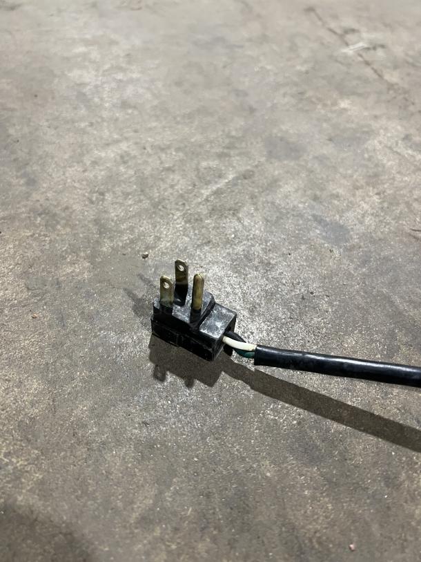 Power plug for Randell commercial refrigerator, model 9302-7, showing three-pronged connector, on a concrete surface.