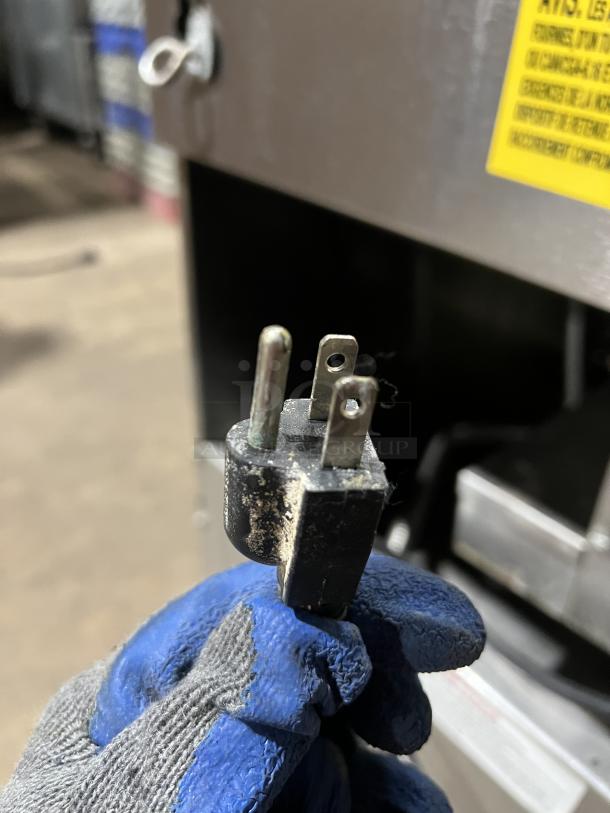 Gloved hand holding a dusty power plug of a Vulcan PowerFry3 commercial fryer, focusing on wear and condition.