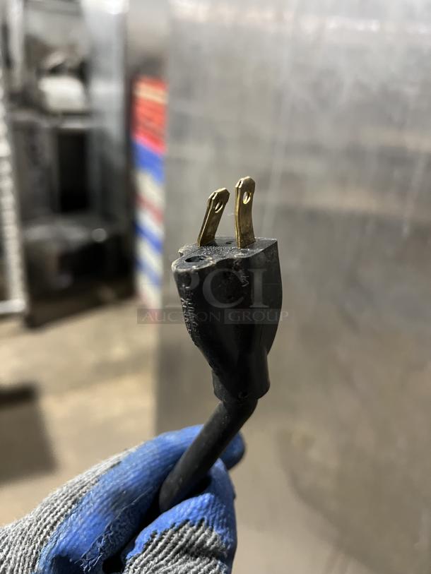 Close-up of a power plug for the FWE PH182618 heated holding cabinet. The plug is black, showing two gold prongs.