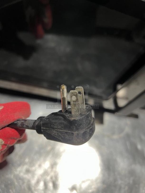 Amana RCS10TS commercial microwave plug. Standard three-prong, shows part of the stainless steel appliance in the background.