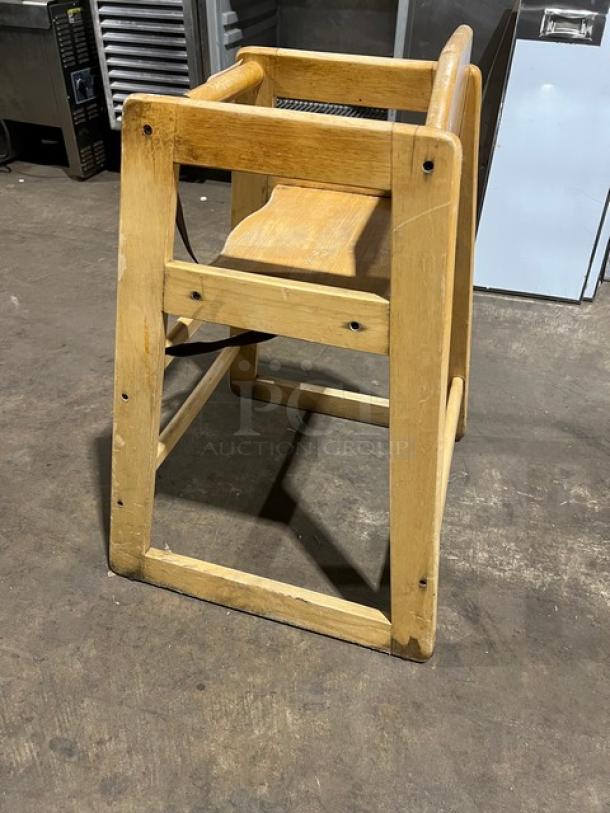 Commercial wooden highchair with safety strap, used condition. Features sturdy wood frame, visible wear marks.