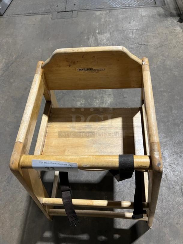 Commercial wooden highchair with safety strap, well-used condition, warning label on backrest. Ideal for restaurants.