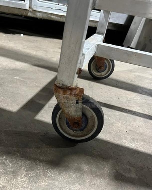 Alexander Industries commercial aluminum 12-pan sheet rack on casters, showing moderate wear and some rust on wheels.