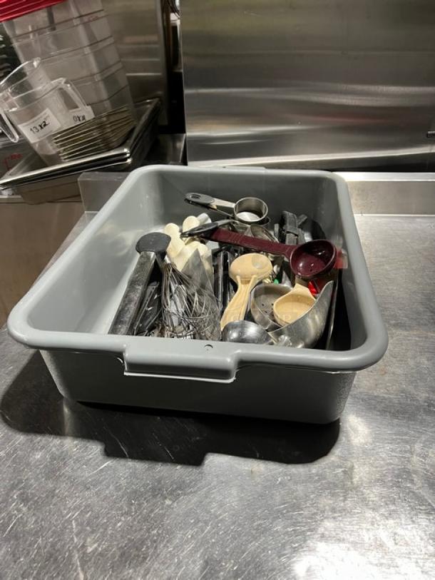 Assorted kitchen utensils in gray bin, includes ladles, measuring spoons, whisks, scoops. Used condition.