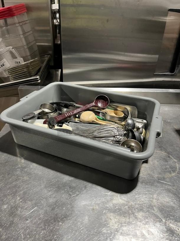 Container of assorted kitchen utensils including measuring spoons, whisks, and ladles. Mixed materials, fair condition.
