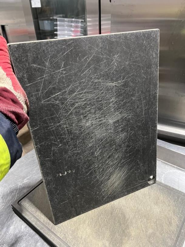 Commercial rectangular cutting board with a well-used, scratched surface, featuring a small hole for hanging.