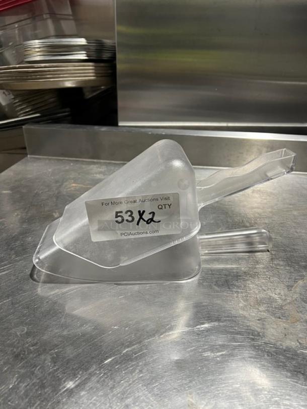 Clear handheld scoop on metal surface; features ergonomic handle and spout. Tag reads "53X2 QTY, PCAuctions.com."