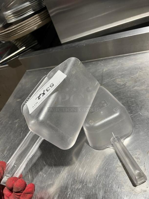 Clear handheld scoop, commercial-grade, plastic material, two included. Price tag reads "2X" on one scoop. Suitable for kitchen use.