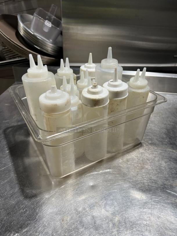 Lot of clear condiment sauce squeeze bottles with lids, used condition, varying sizes in a storage container.