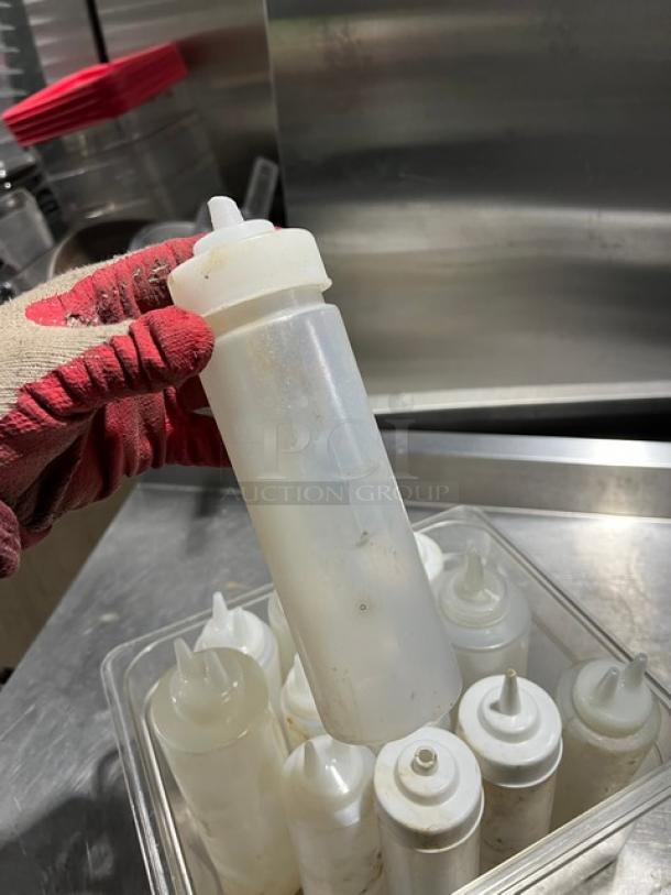 Lot of clear condiment squeeze bottles with lids; used condition, suitable for sauces or dressings.