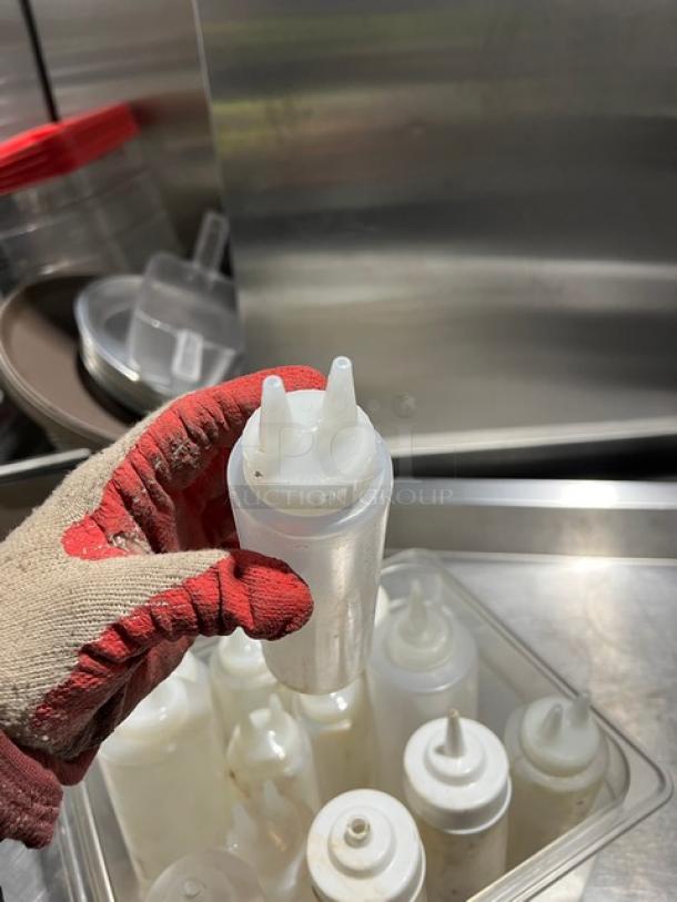 Lot of clear condiment squeeze bottles with lids, various sizes. Used condition, suitable for sauces or dressings.